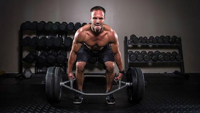 man in gym performing trap bar deadlifts